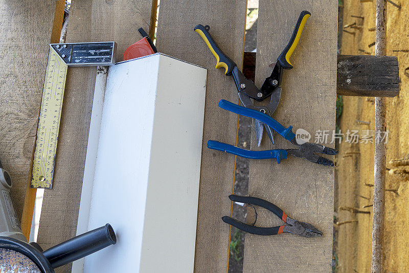 施工工具角磨床，角量尺，钳子，铁剪刀，钻头，卷尺。木脚手架上放着一个工作工具。