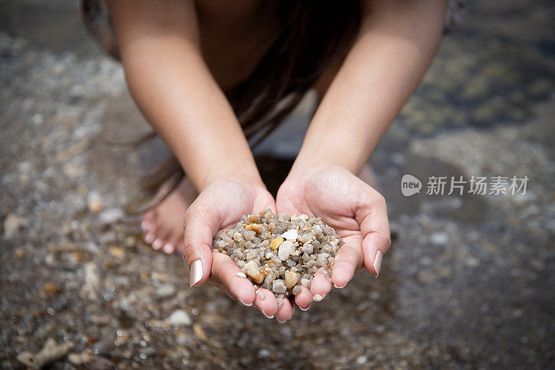 女人手里拿着小石子在沙滩上，靠近了。