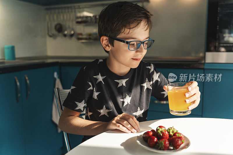 可爱的男孩吃着草莓喝着果汁
