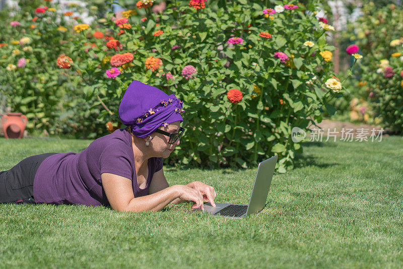 一个成熟的女人躺在草地上用笔记本电脑