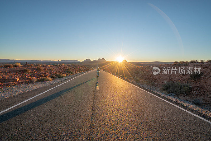 后视图的妇女走在漫长的高速公路上通往纪念碑谷在美国。人们在美国旅行的概念