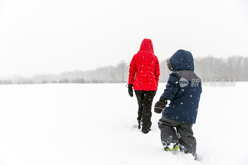 母亲和儿子走在田野在冬天暴风雪期间