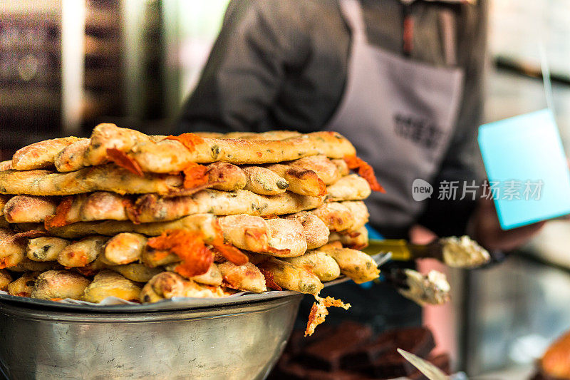 一堆新鲜烘焙的手工面包和佛卡夏面包，面包师在食品市场的背景