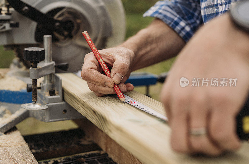 近距离男子测量木板和建立木制露台甲板在他的房子与圆锯工具