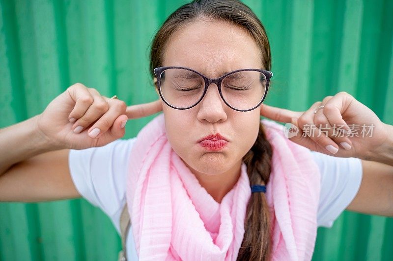 顽皮的女人与手指在耳朵里扮鬼脸绿色背景-股票照片