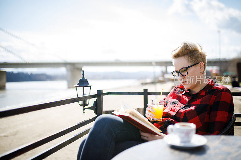 一位美丽的年轻女子坐在河边的咖啡馆里看书