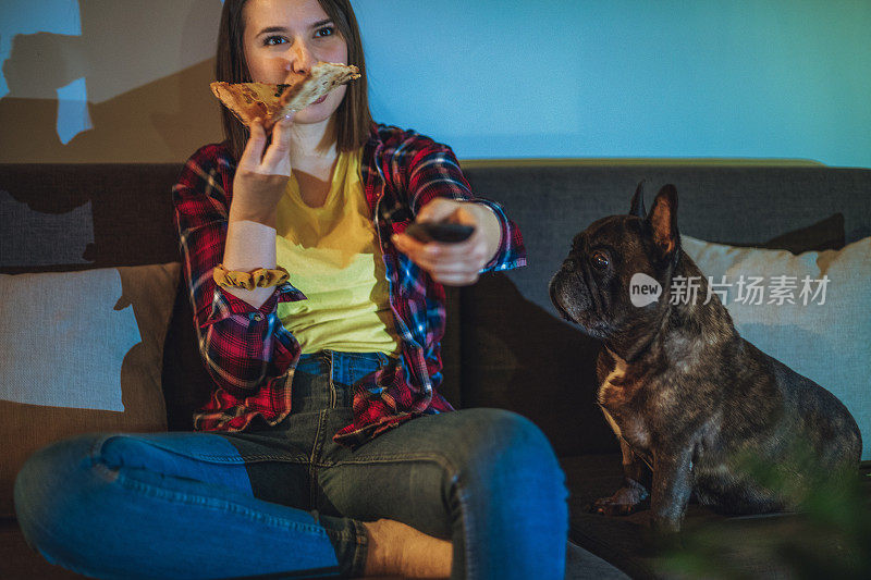 一个女人在沙发上吃披萨，和她的狗一起看电视