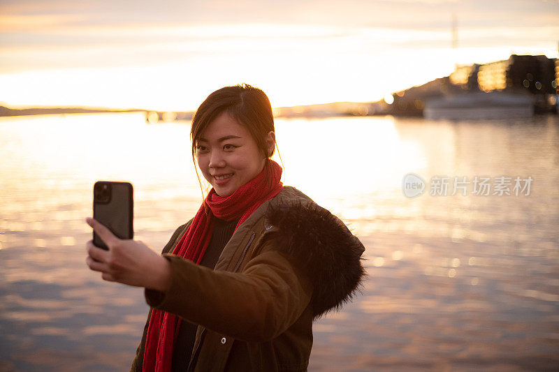 快乐的亚洲女人自拍与智能手机在日落的风景