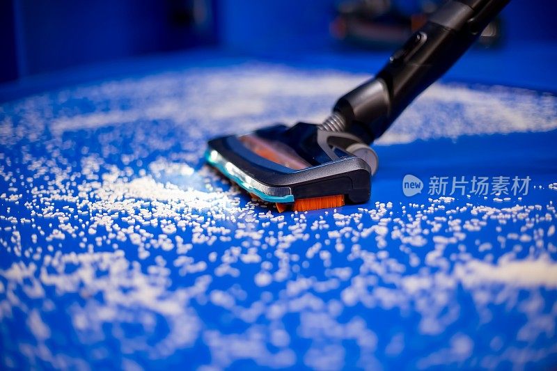 一种新的带湿式清洁和led的真空吸尘器可以清除蓝色地板上的白色碎屑。特写，柔焦