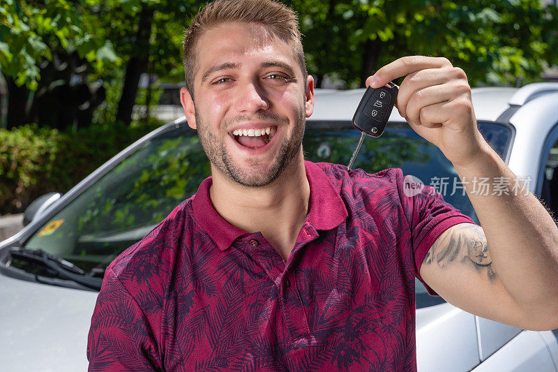 快乐的年轻人在银色汽车前展示新的汽车钥匙