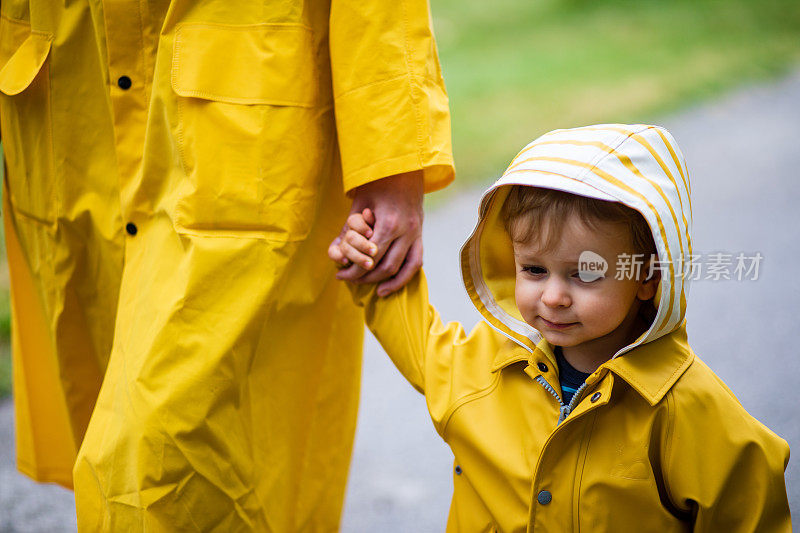 母亲和蹒跚学步的孩子，男孩，在雨中玩耍，穿着靴子和雨衣