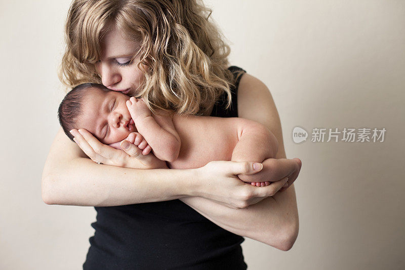 慈爱的母亲抱着并亲吻新生的婴儿