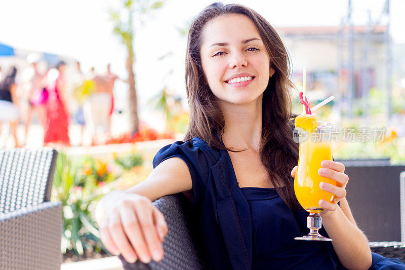 喝着橙汁坐在户外夏日咖啡馆里的年轻女子