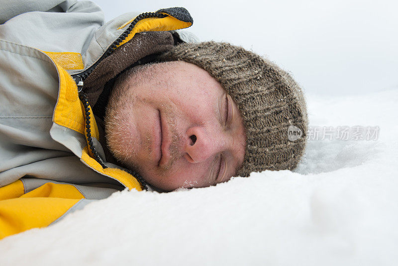 疲惫的男人穿着冬衣和帽子躺在雪地里