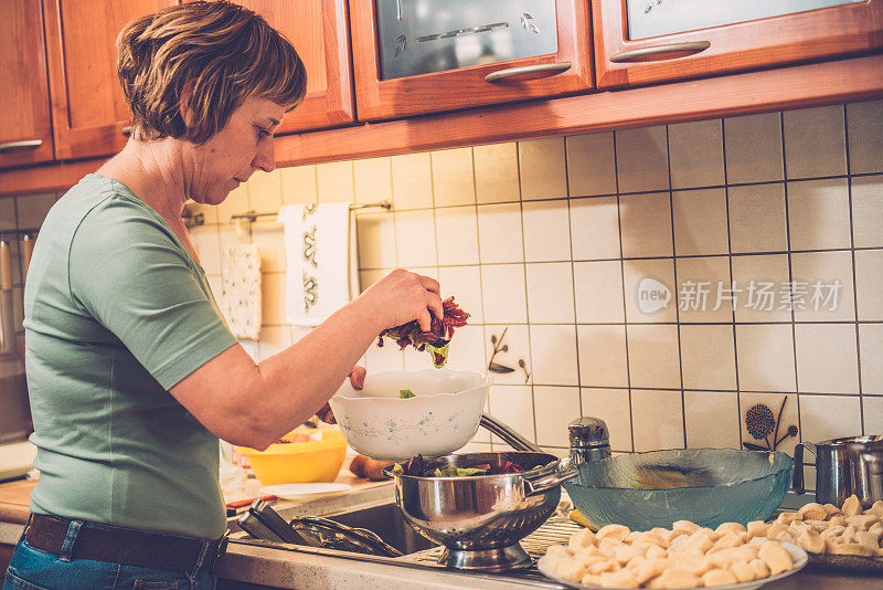 穿着牛仔裤的女人在洗涤槽里洗菊苣，家庭厨房，欧洲