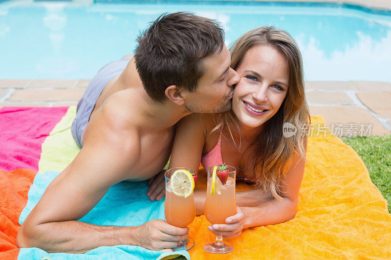 一个男人躺在泳池边的毯子上亲吻一个女人