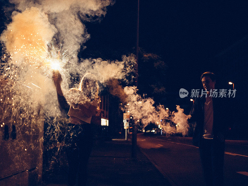 一对年轻夫妇在城市街道上玩烟雾弹和烟火