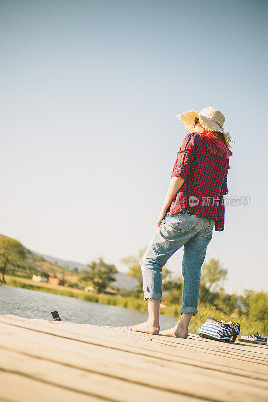 美丽的女人站在户外湖边的木码头上