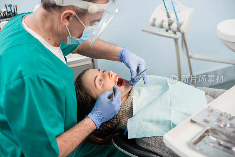 男性牙医使用牙科工具-镜子和探针在牙科诊所治疗病人的牙齿。医学、牙科和保健概念。牙科设备