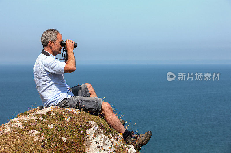 成熟的人在海岸悬崖上用双筒望远镜观鸟