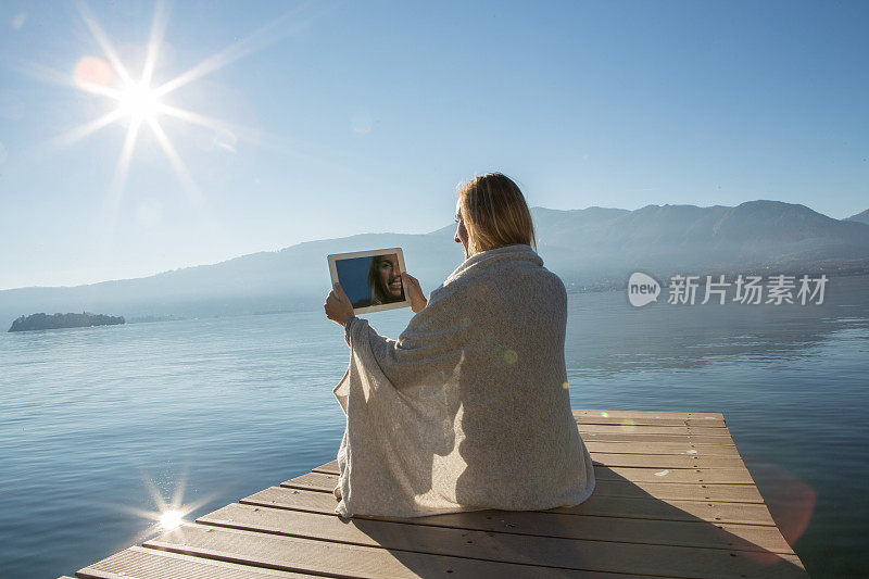 年轻女子在湖边码头上玩着平板电脑