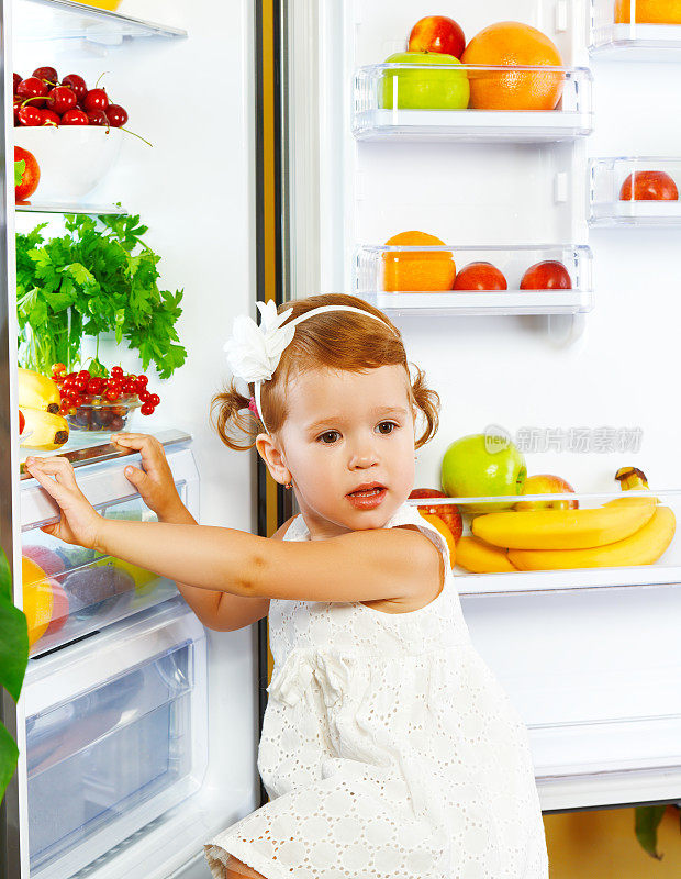 快乐的小女孩在冰箱旁边放着健康的食物，水果