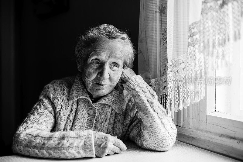一位老妇人坐在桌旁，一张黑白照片。