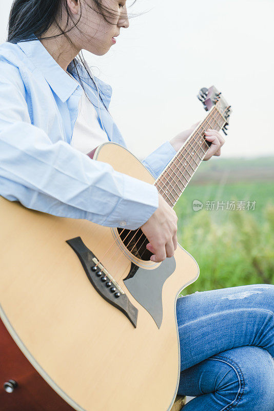 女人的手在田野里弹吉他的特写