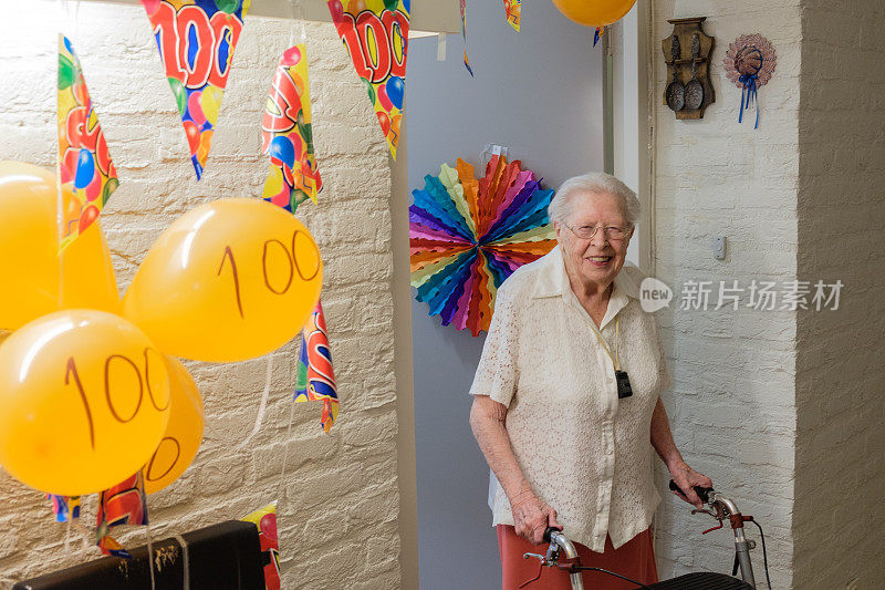 一位老妇人站在她装饰过的房间门前庆祝她的百岁生日