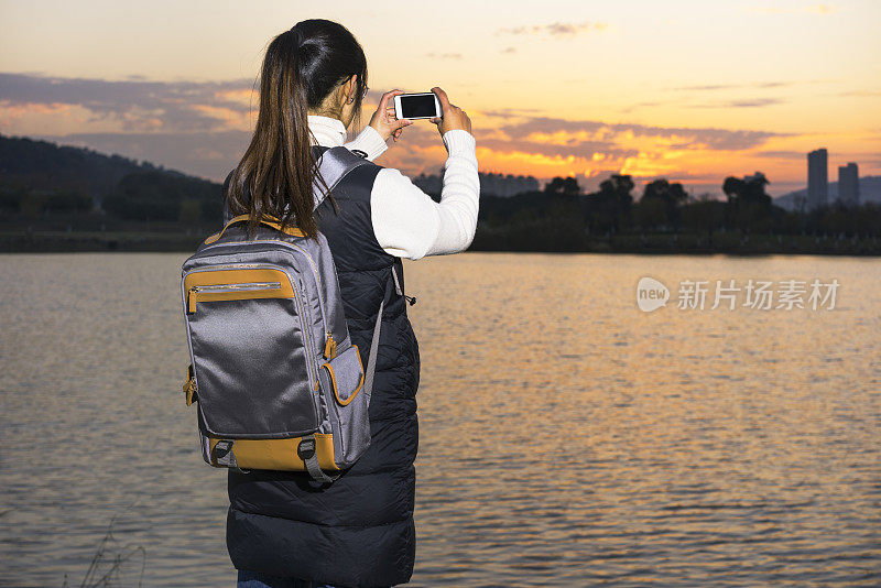 一个女人站在码头上用智能手机拍照