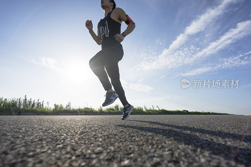 年轻的男运动员在柏油路上迎着天空奔跑