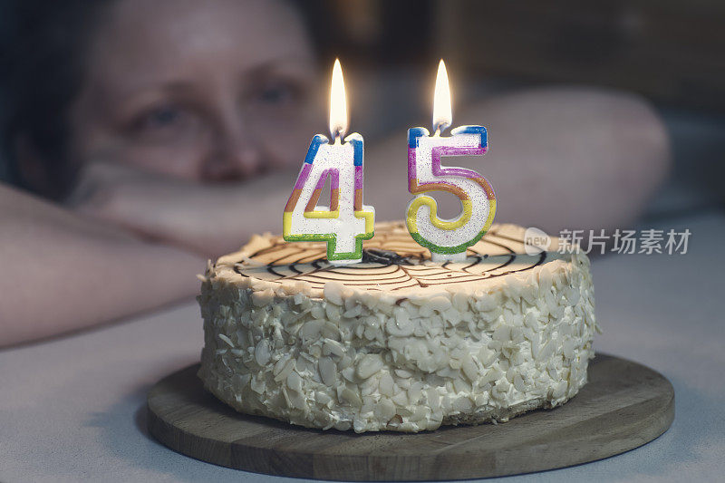 女人看不年轻的蛋糕，蜡烛都以数字45的形式燃烧着