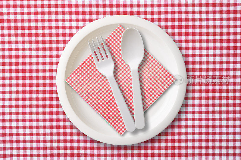 红色格子布桌布上的白色塑料盘子和勺子