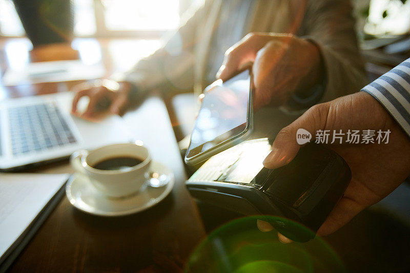 近场通信(NFC)支付:特写镜头中，一位面面相觑的女商人在咖啡馆里买咖啡时，将现代智能手机放到读卡器上
