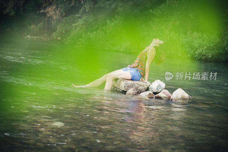 女孩坐在河里的一块石头上