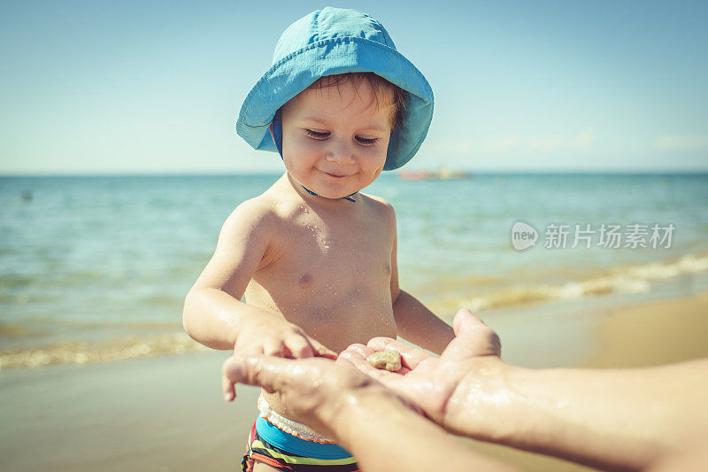 可爱的小男孩在海滩上玩贝壳和石头