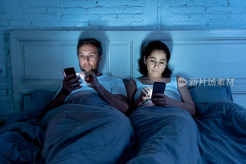 年轻夫妇在床上玩手机，沉迷于游戏、社交媒体和应用程序，忽视了彼此的关系沟通问题和互联网移动成瘾的概念。