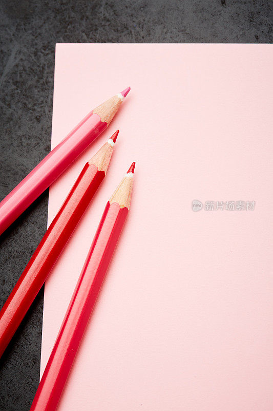 三支红色蜡笔在空白的粉色记事本上