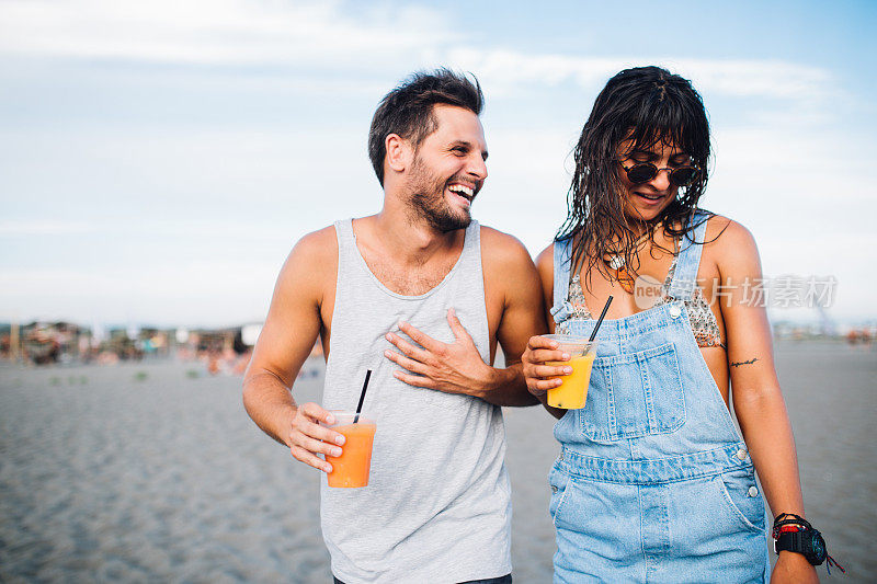 年轻的夫妇有乐趣和喝鸡尾酒在海滩上