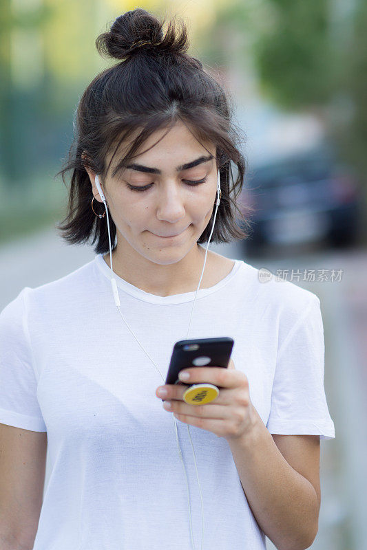 一个穿着运动服的年轻女子正在室外听手机里的音乐