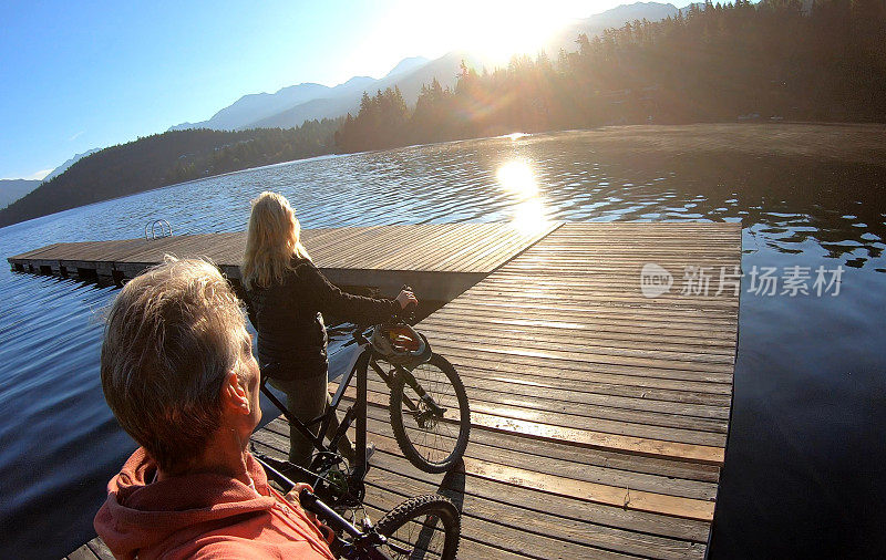一对夫妇在日出时沿着湖边的码头骑自行车