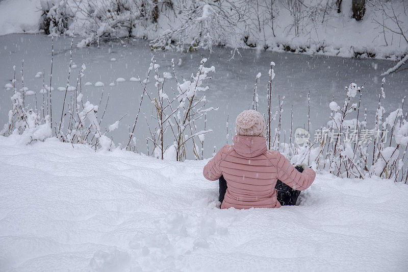 女徒步旅行者在白雪覆盖的河岸放松