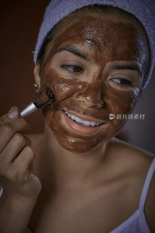 近距离的西班牙年轻女子在洗澡后敷巧克力面膜在她的脸上