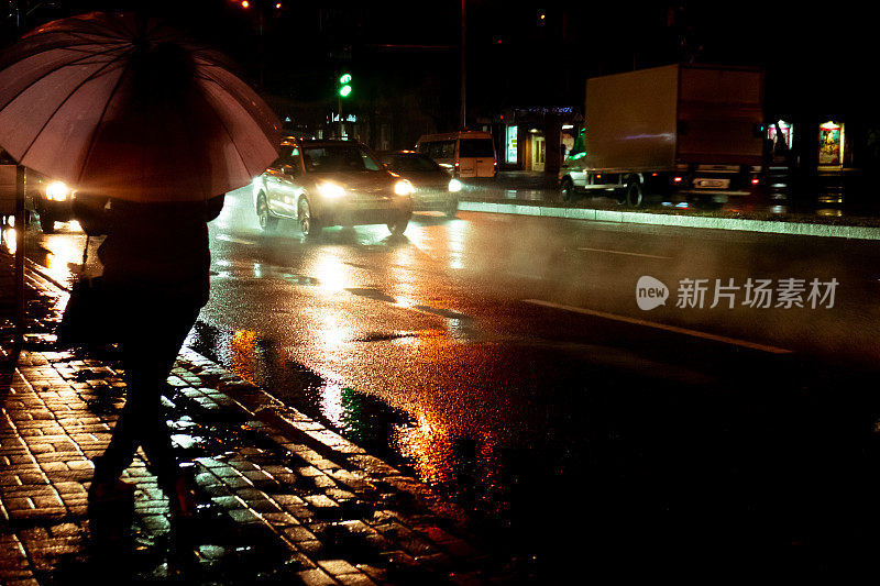 下雨的晚上。一个女人撑着伞，在车流中落下雨滴。