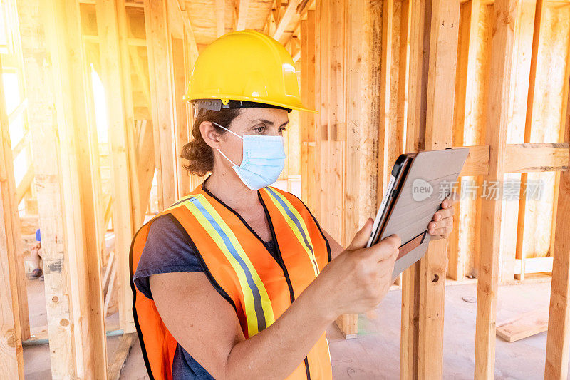 成熟的女建筑工人戴着防护面罩看着她的数字平板电脑