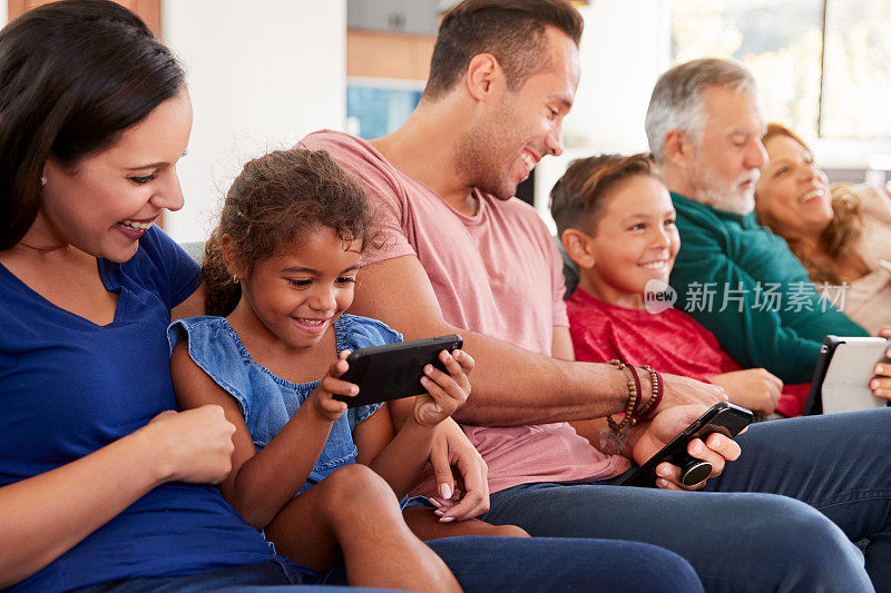 坐在沙发上看电视、玩平板电脑和手机的几代同堂家庭