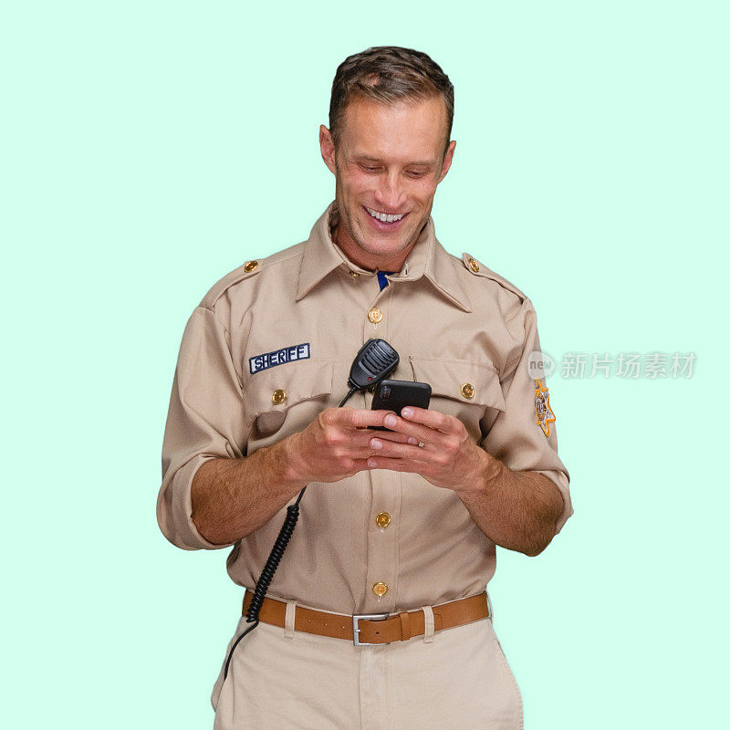 白人男性警察站在有色背景下佩戴警徽并使用短信