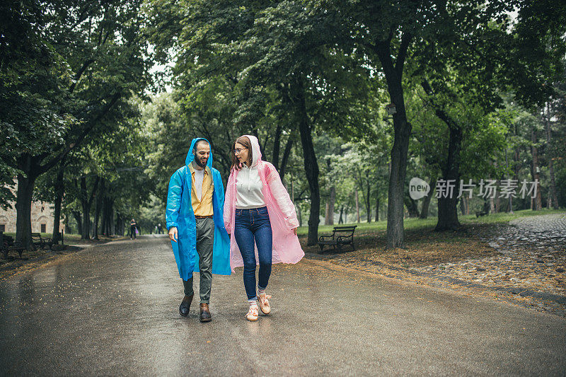 快乐的年轻夫妇在雨中在公园里穿着雨衣