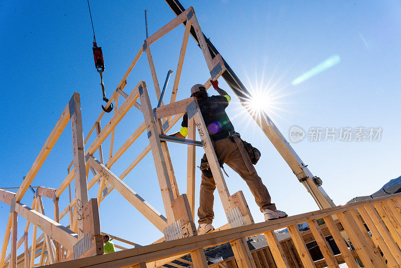 一个构架师站在一个新房屋建筑的骨架墙上，指导起重机操作员安装另一个桁架