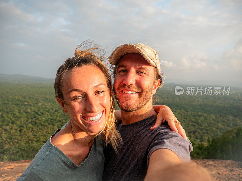 日落时分，一对年轻夫妇在岩石上用手机自拍